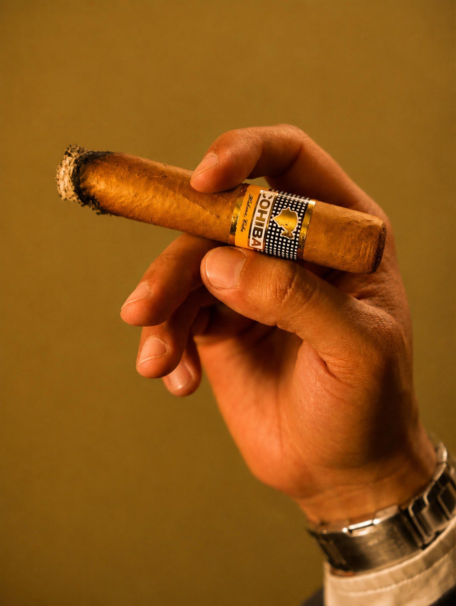 Mano sosteniendo un habano encendido sobre fondo dorado