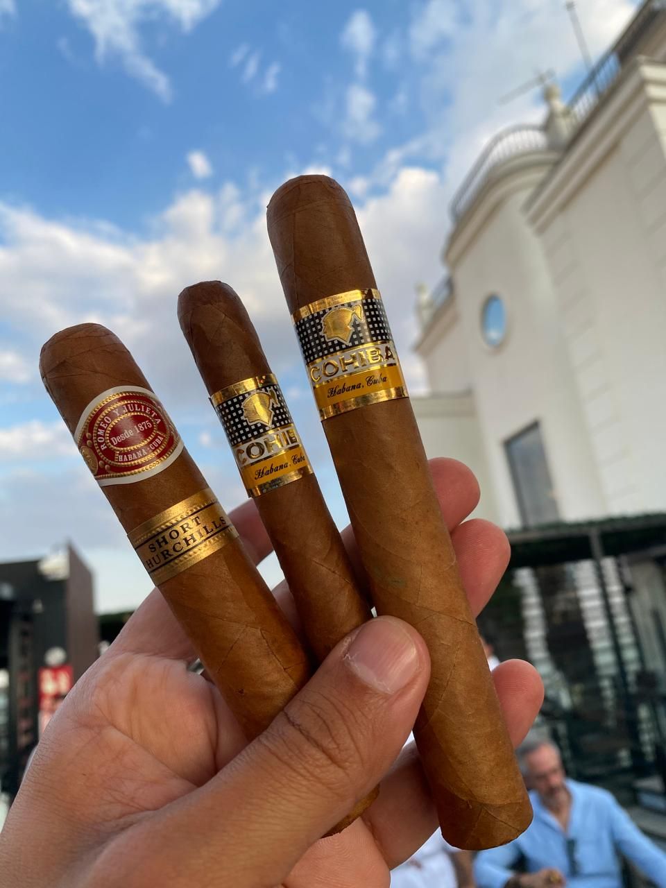 Tres habanos sostenidos en la mano contra el cielo